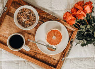 A wooden tray with coffee, grapefruit, and oatmeal, resting on a bed with a white bedspread.