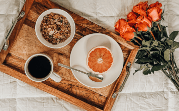 A wooden tray with coffee, grapefruit, and oatmeal, resting on a bed with a white bedspread.
