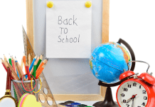 A desk with a small globe, alarm clock, a pencil holder full of colored pencils, and a sign that states 'back-to-school'
