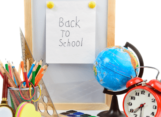 A desk with a small globe, alarm clock, a pencil holder full of colored pencils, and a sign that states 'back-to-school'