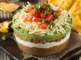 a picture of bean dip, topped with guacamole, cheese, and tomatoes with a side of chips