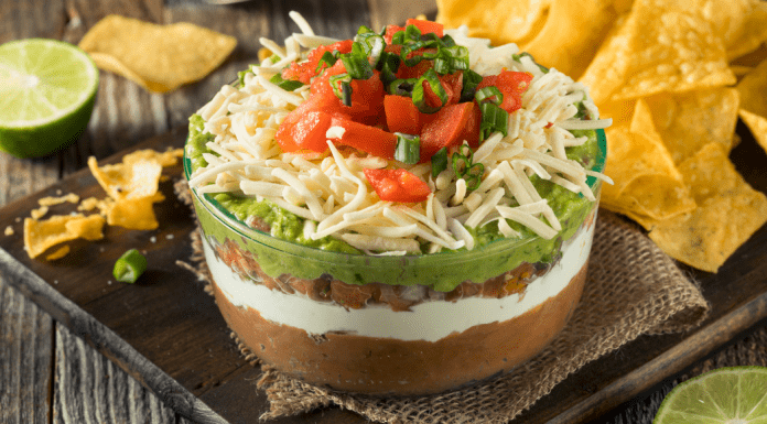a picture of bean dip, topped with guacamole, cheese, and tomatoes with a side of chips