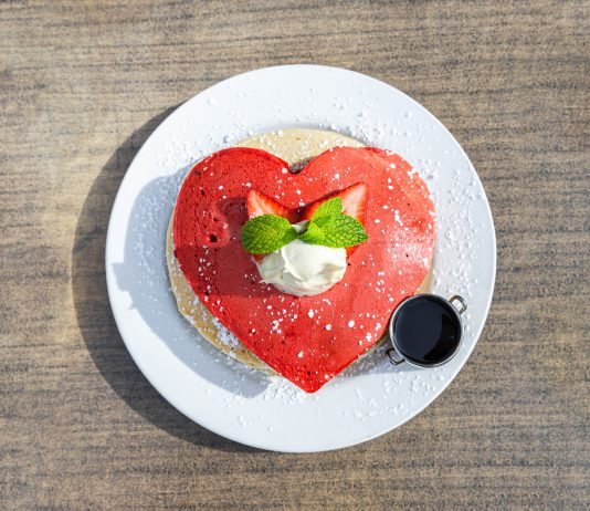 A plate piled high with red heart pancakes and a side of syrup.
